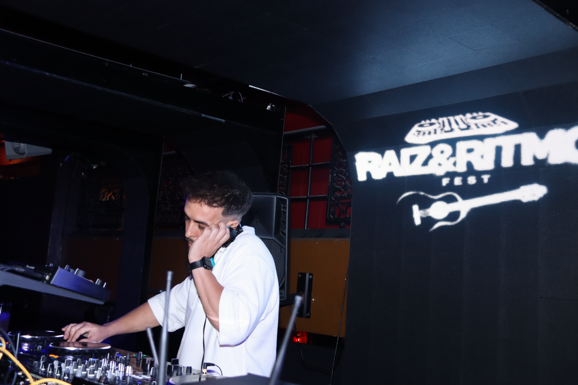DJ en cabina con pantalla del logo Raíz & Ritmo Fest al fondo