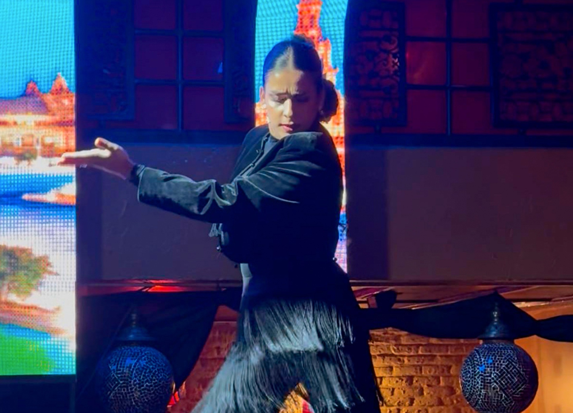 Bailaora flamenca con traje de flecos negro sobre escenario con pantallas LED